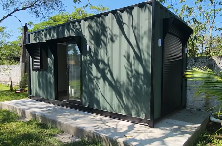 Fachada do container 15 m² em verde musgo com porta de vidro e persiana preta